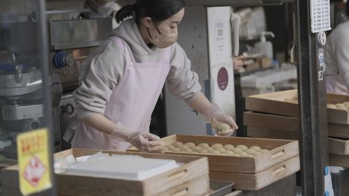 Free Asian woman working in a bakery, arranging baked goods into wooden trays. Stock Photo