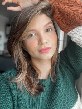 A woman with makeup wearing a color-block sweater, posing indoors with a bright expression.