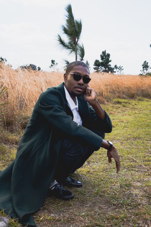 Free Fashionable man in sunglasses crouching in a grassy park, exuding confidence and style. Stock Photo