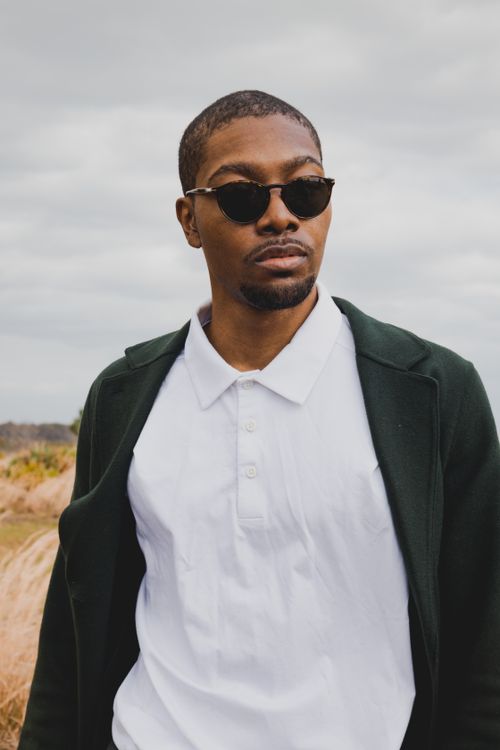 Free A fashionable man wearing sunglasses enjoying a breezy outdoor day, embodying contemporary style. Stock Photo