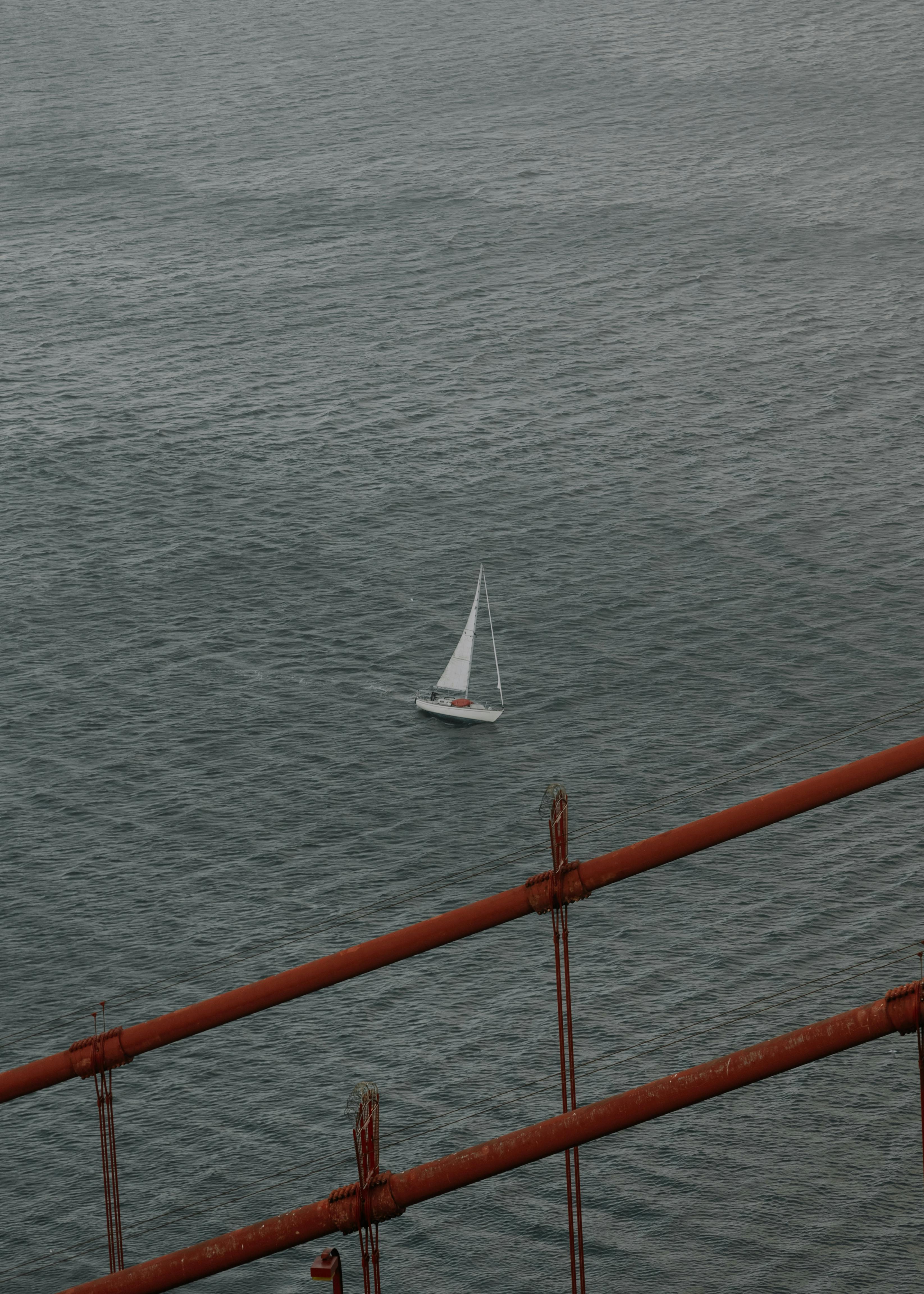 A serene view of a sailboat gliding near a rusty bridge in San Francisco.