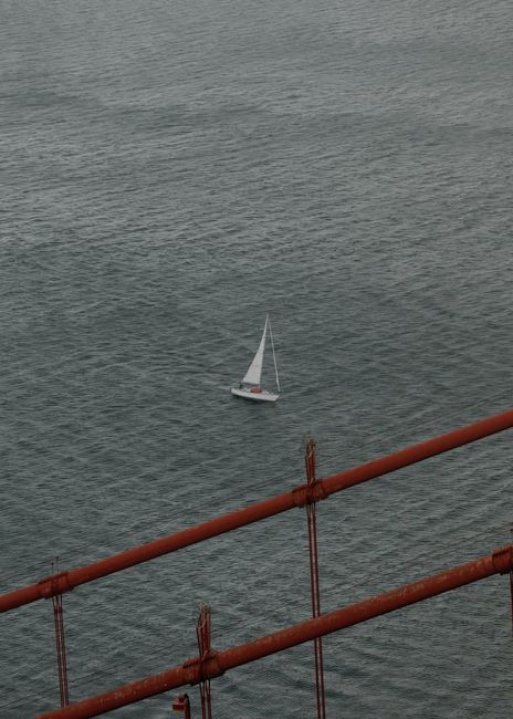 A serene view of a sailboat gliding near a rusty bridge in San Francisco.