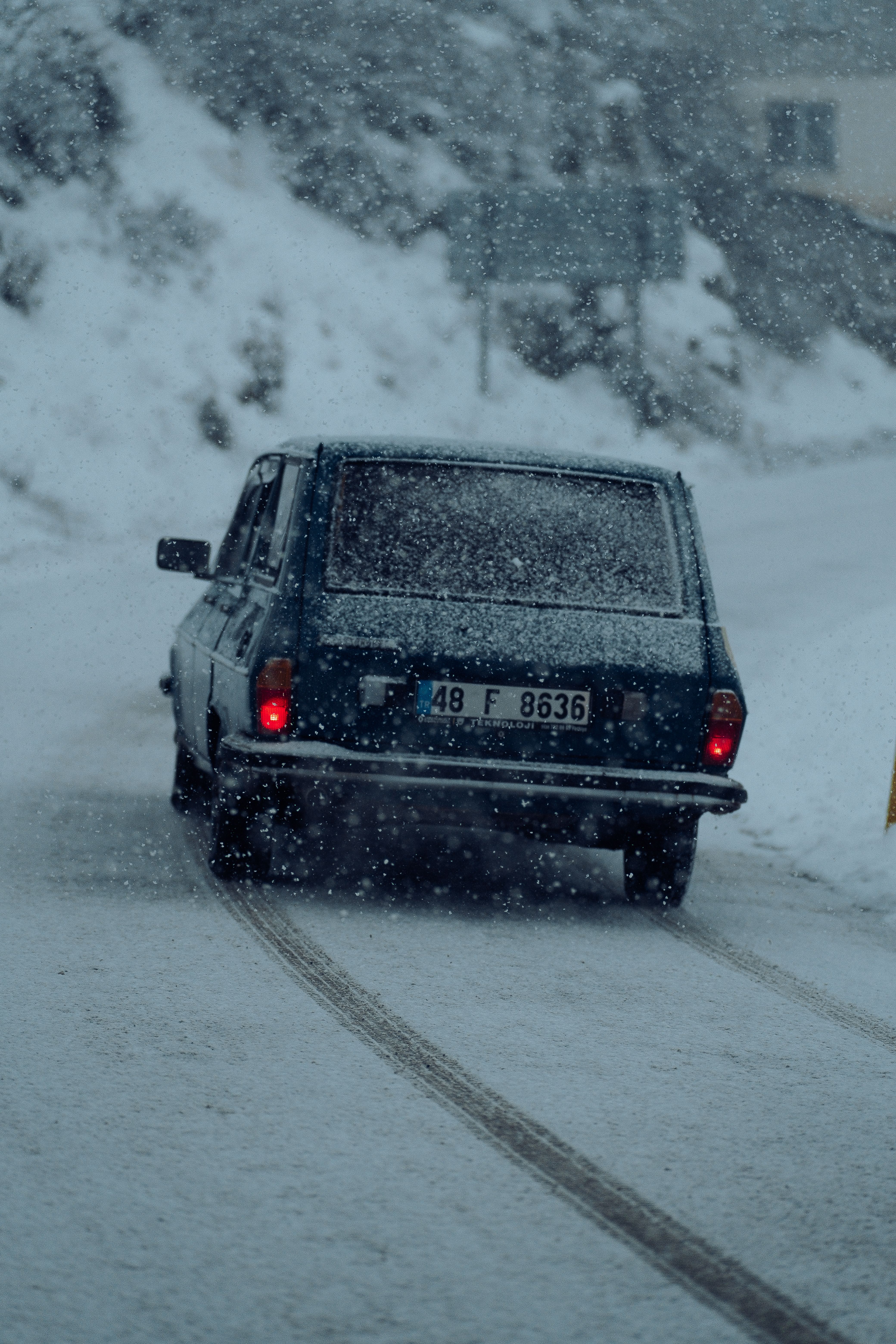 A vintage car navigates a snowy, slippery road during a winter snowstorm.