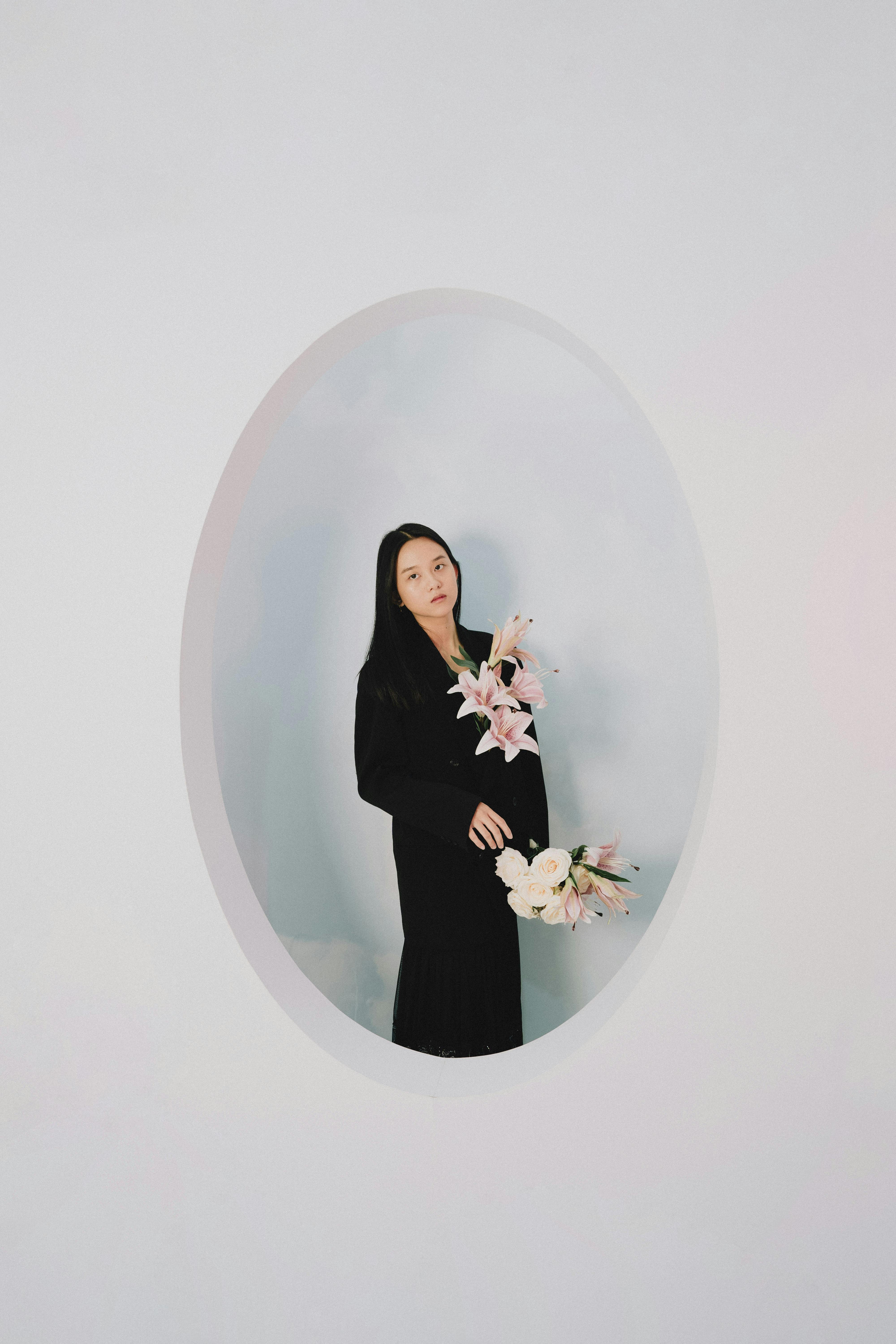 Minimalist portrait of a woman holding flowers in an oval frame.