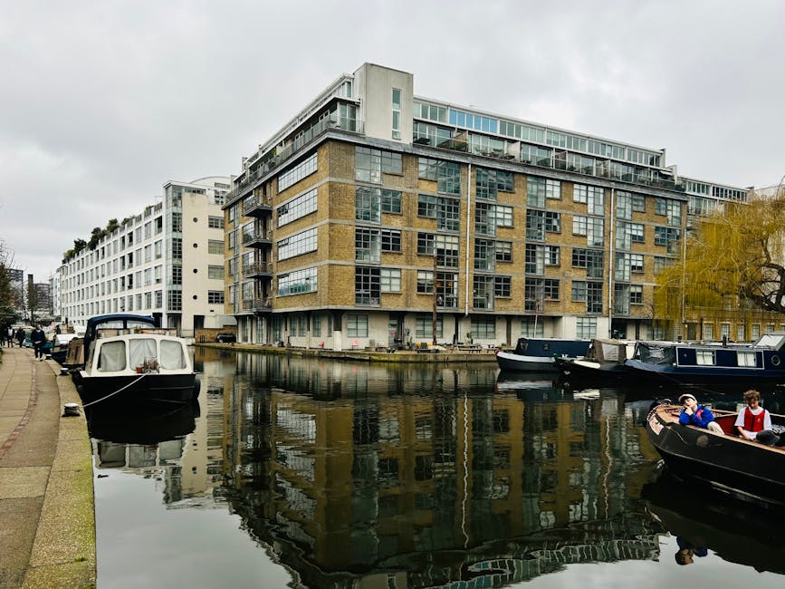 Contemporary buildings reflected on a canal with boats docked along the shore.