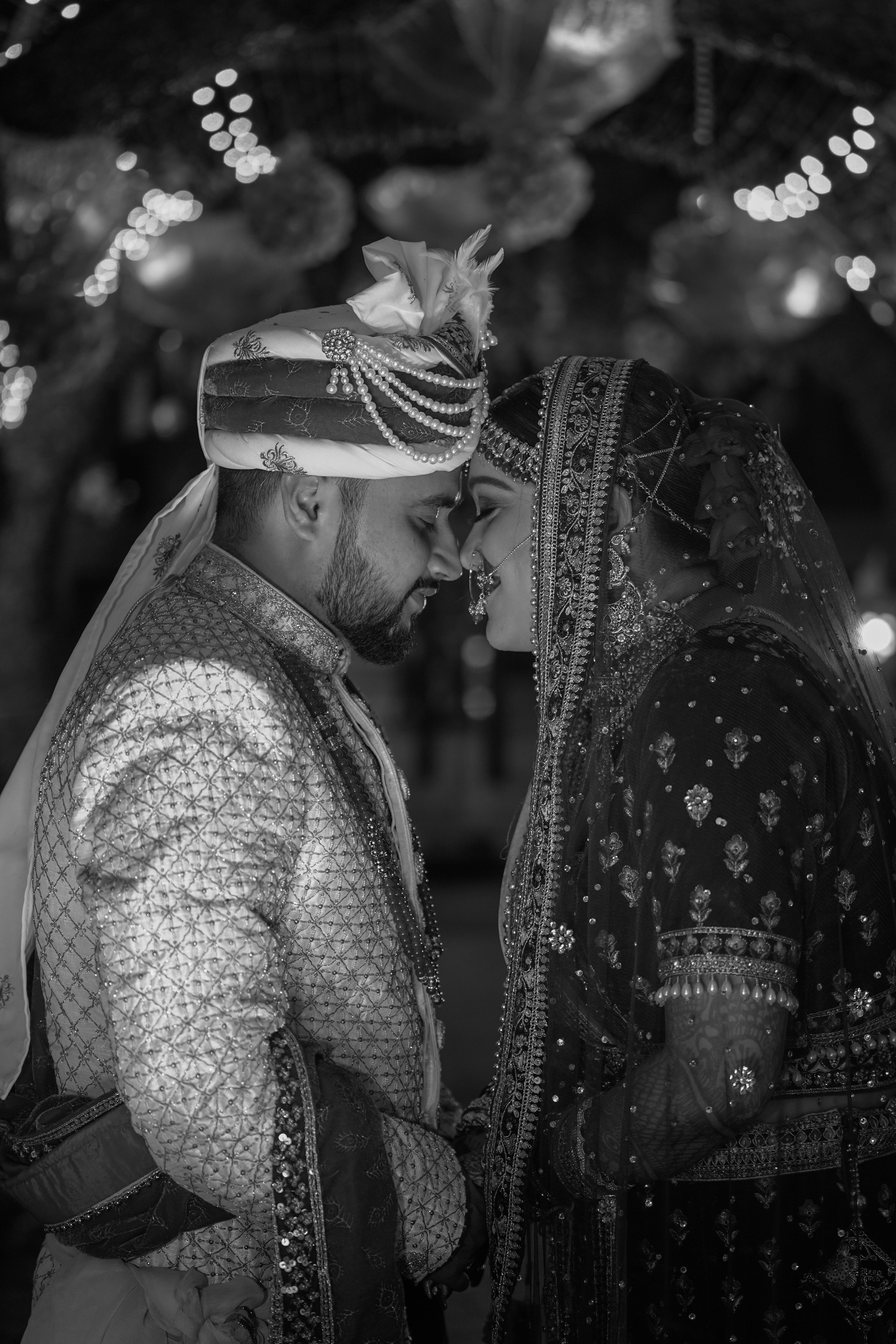 A couple in traditional Indian wedding attire, embracing lovingly in black and white.