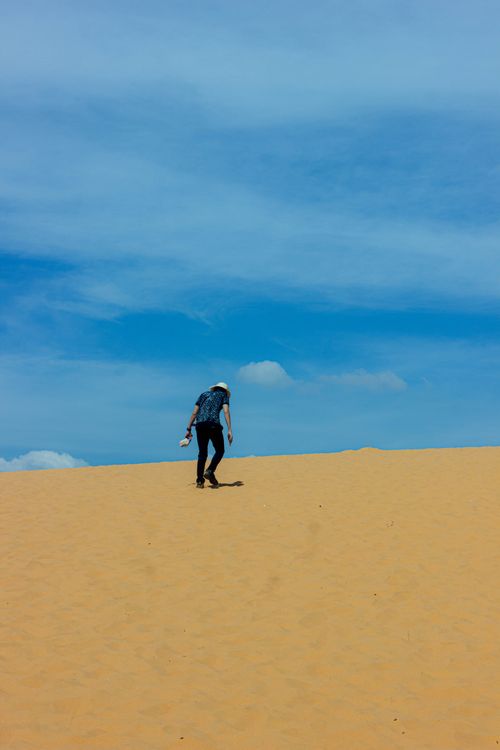 Free A solitary figure walks up vast sunlit sand dunes under a clear blue sky, showcasing adventure. Stock Photo