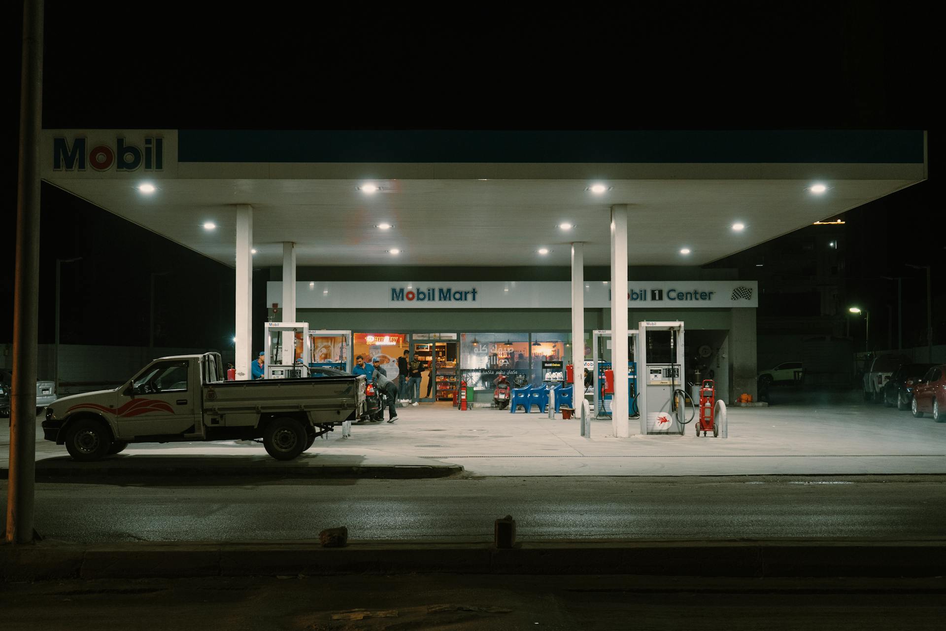 A Mobil gas station with vehicles and people under bright lights at night.