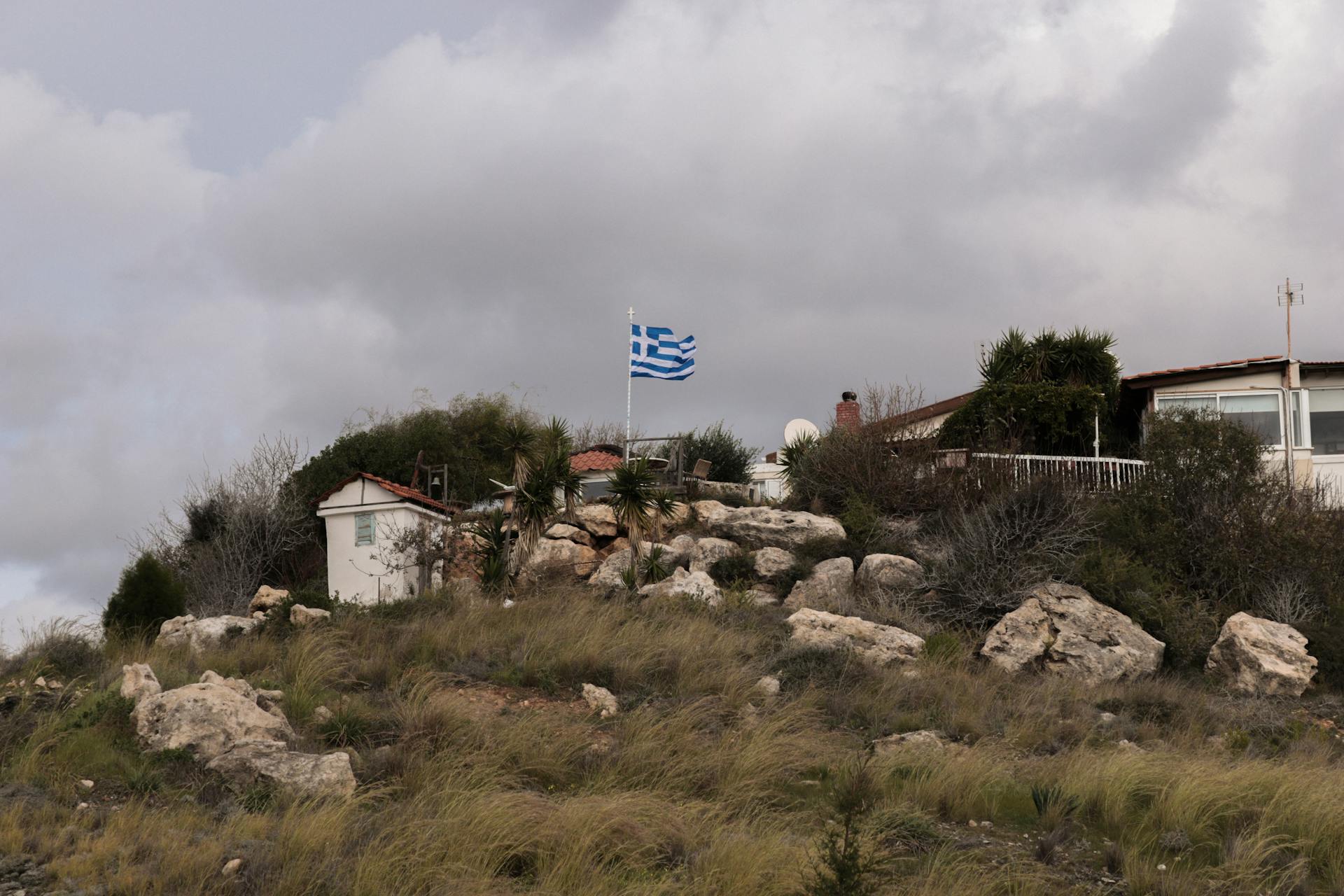 Charming rural landscape with a Greek flag on a rocky hill in Paphos, Cyprus.