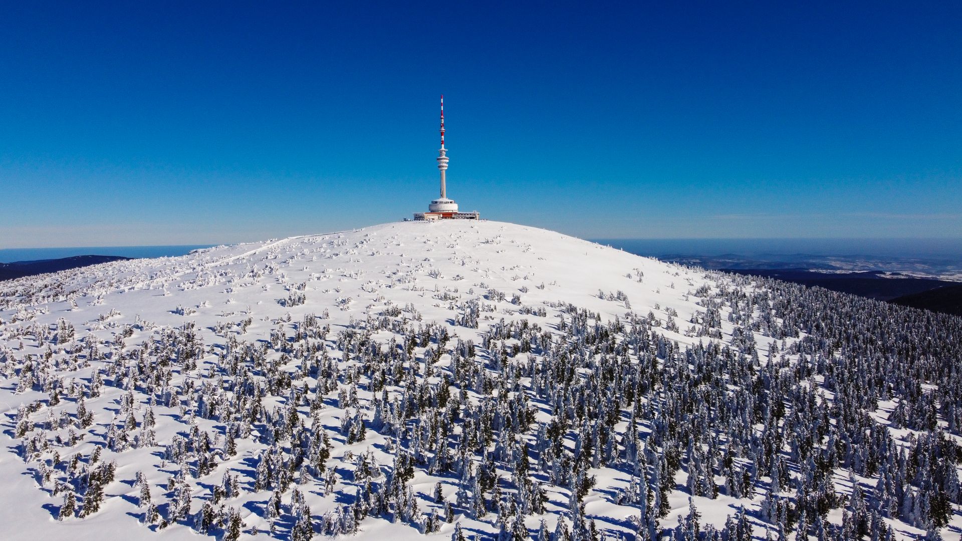 Explore the scenic snow-blanketed landscape featuring a prominent television transmitter on a sunny winter day.