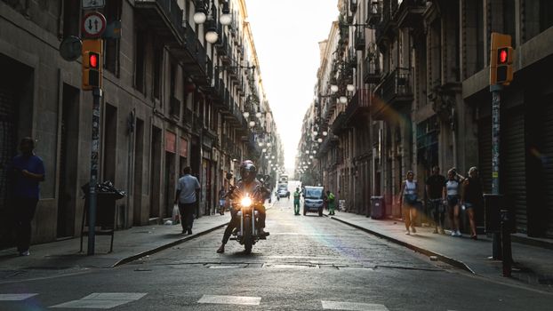 A motorcyclist rides through a sunlit historic street in Barcelona, Spain, capturing urban life.