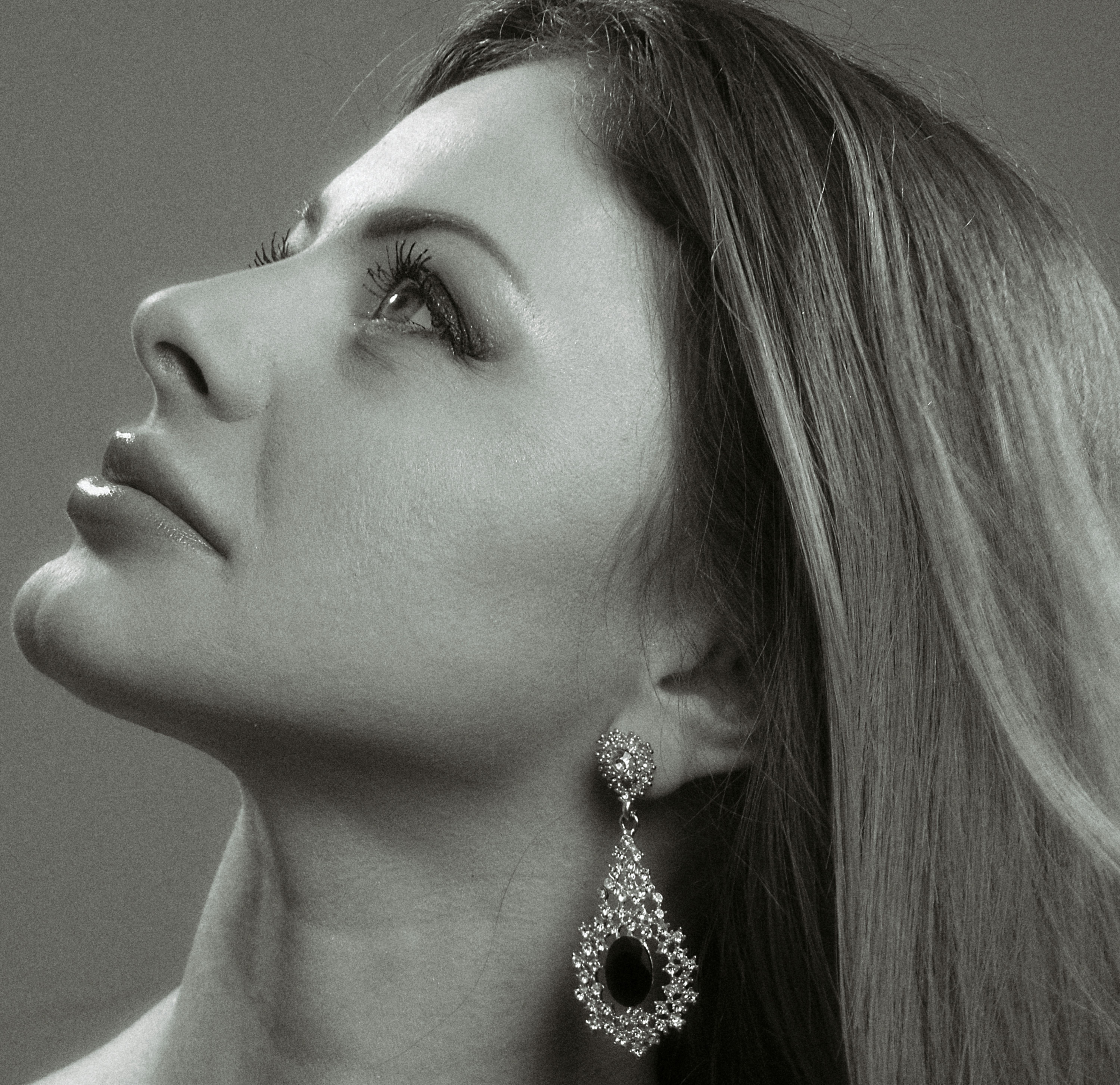 Elegant black and white headshot of a woman with long hair looking upwards.
