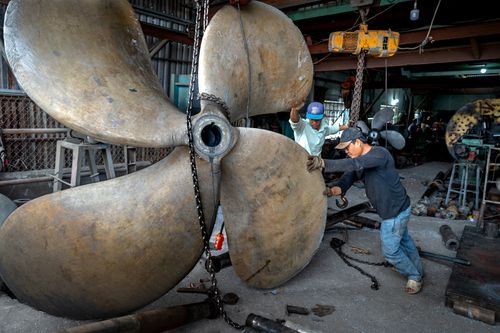 Free Two men working together to handle a massive industrial propeller in a workshop setting. Stock Photo