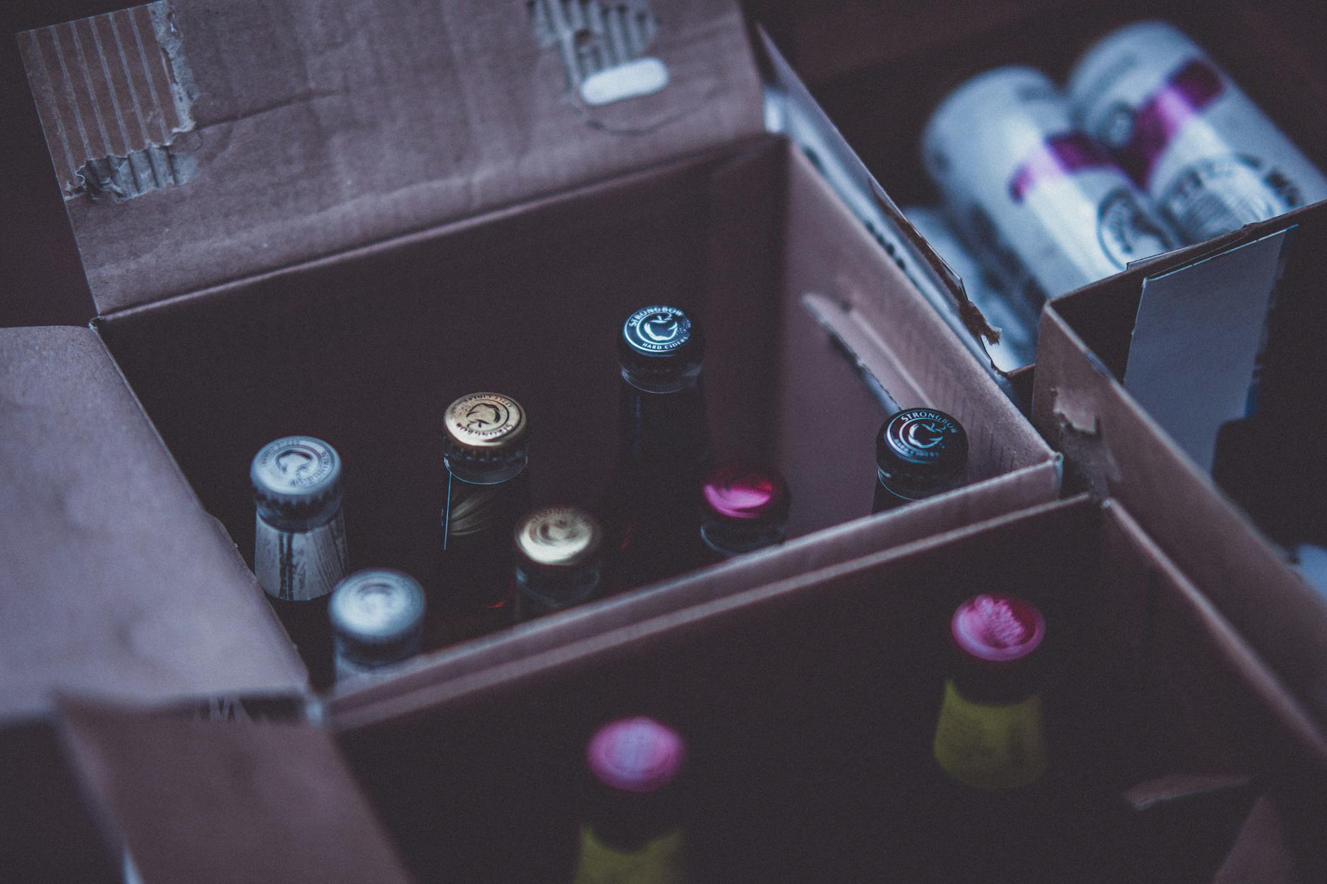 Close-up of various alcohol bottles and cans in cardboard boxes indoors.