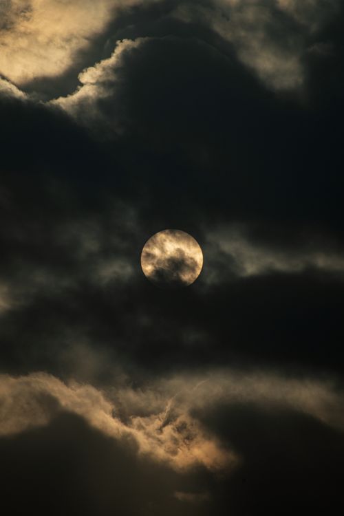Free A haunting full moon partially obscured by clouds creating an atmospheric night scene over Mashhad, Iran. Stock Photo