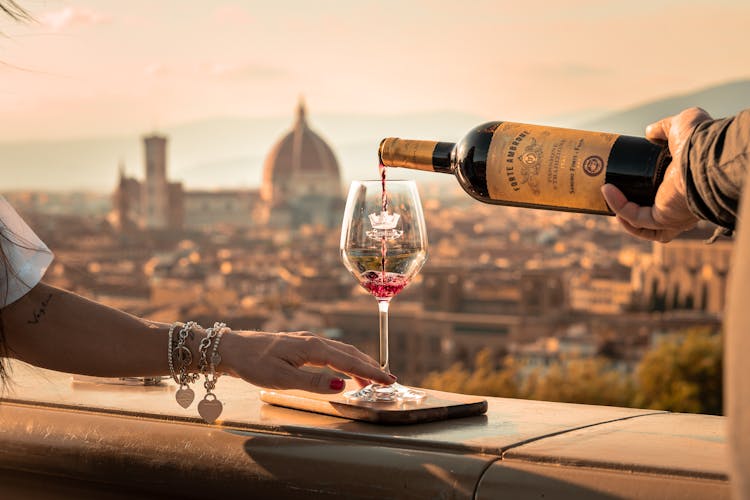 Pouring Wine To Woman Glass In Sunlight And With Town Behind