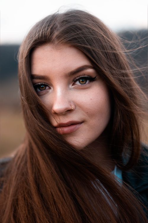 Free Close-up portrait of a young woman with long hair and nose ring, smiling outdoors. Stock Photo