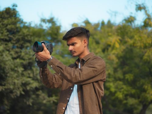 Free A young man focuses his camera amidst a lush green background, embracing the beauty of nature. Stock Photo