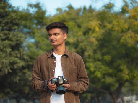 A young male photographer with a DSLR camera standing in a green park during daytime.