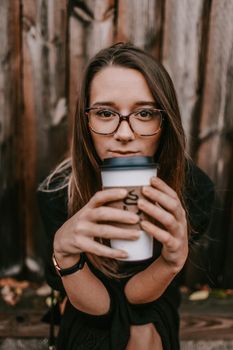 一位戴眼镜的年轻女子在户外木栅栏旁拿着咖啡杯
