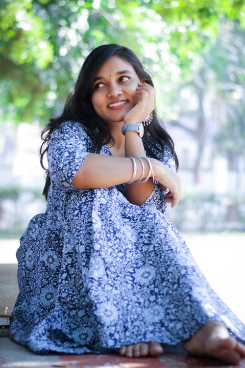 Free A smiling woman in a blue floral dress sits outdoors, enjoying the bright day. Stock Photo