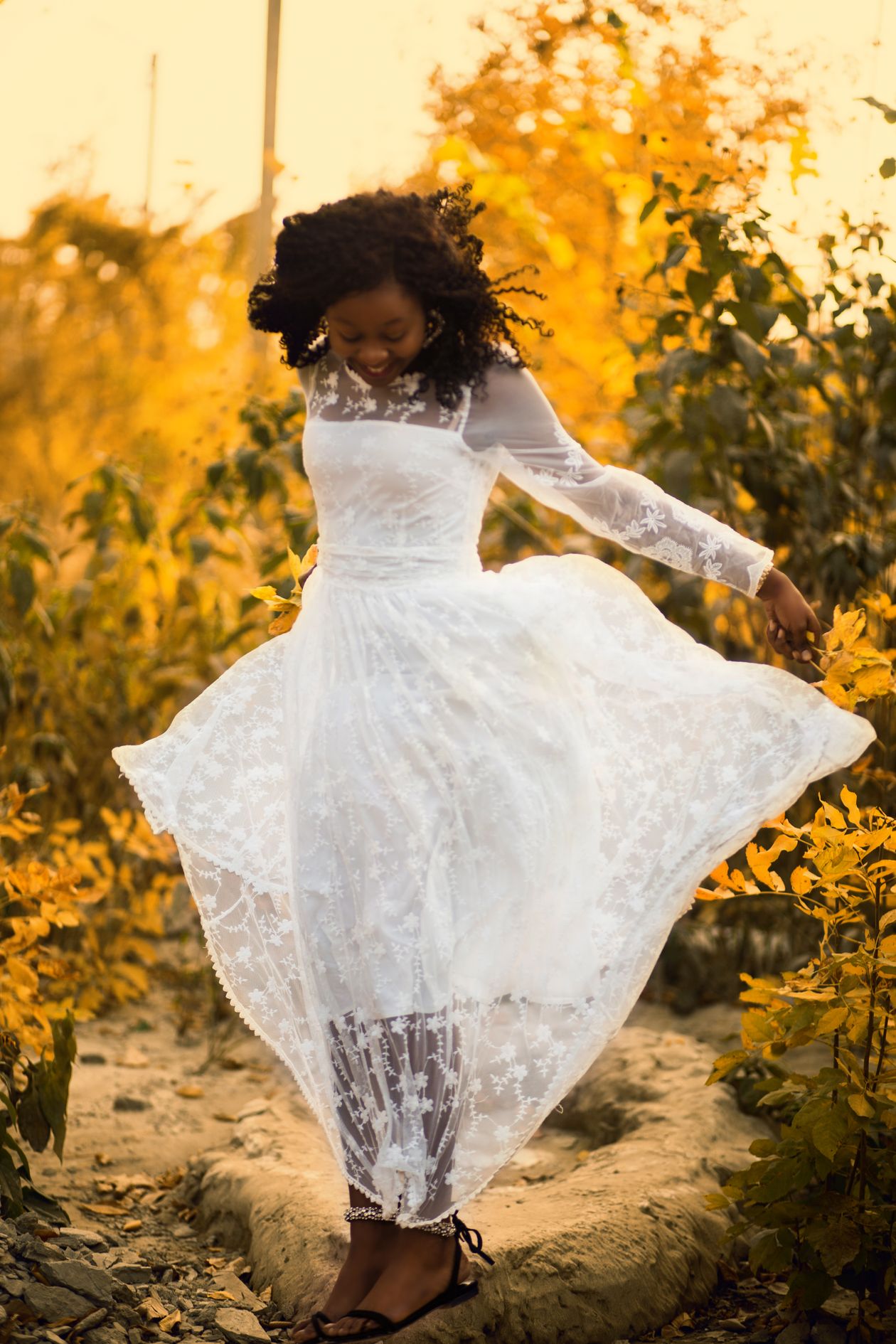 Woman twirling in a white lace dress with sheer sleeves among autumn leaves