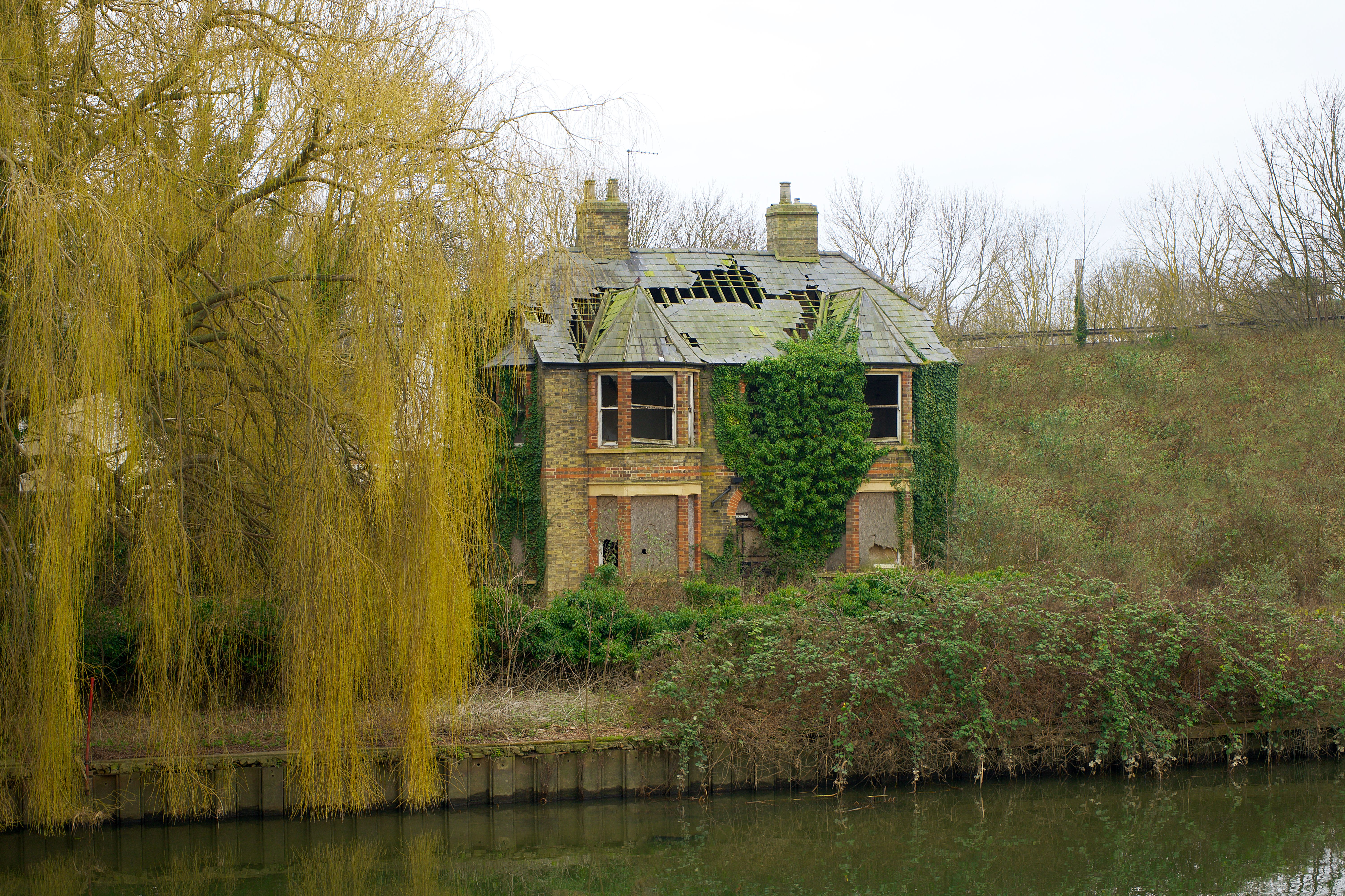 A scenic view of an abandoned house covered in ivy by the river in Godmanchester, England.