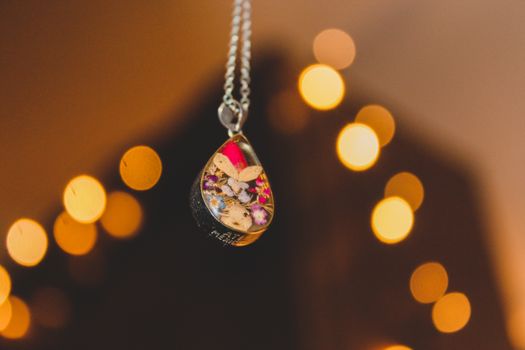 A close-up of a handmade pendant with flowers and leaves, featuring a warm bokeh background.