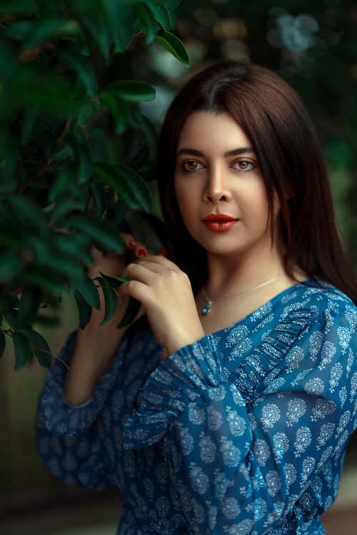 Free A beautiful woman in a blue dress posing thoughtfully, surrounded by greenery. Stock Photo