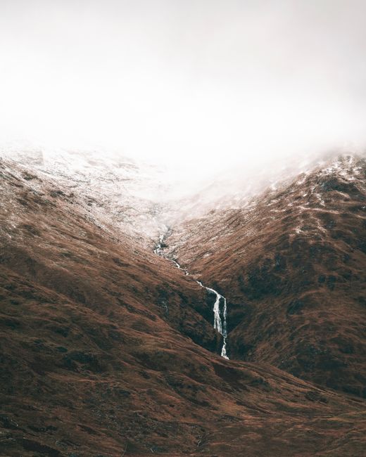 A tranquil scene of snow-dusted mountains and a cascading waterfall under a cloudy sky.