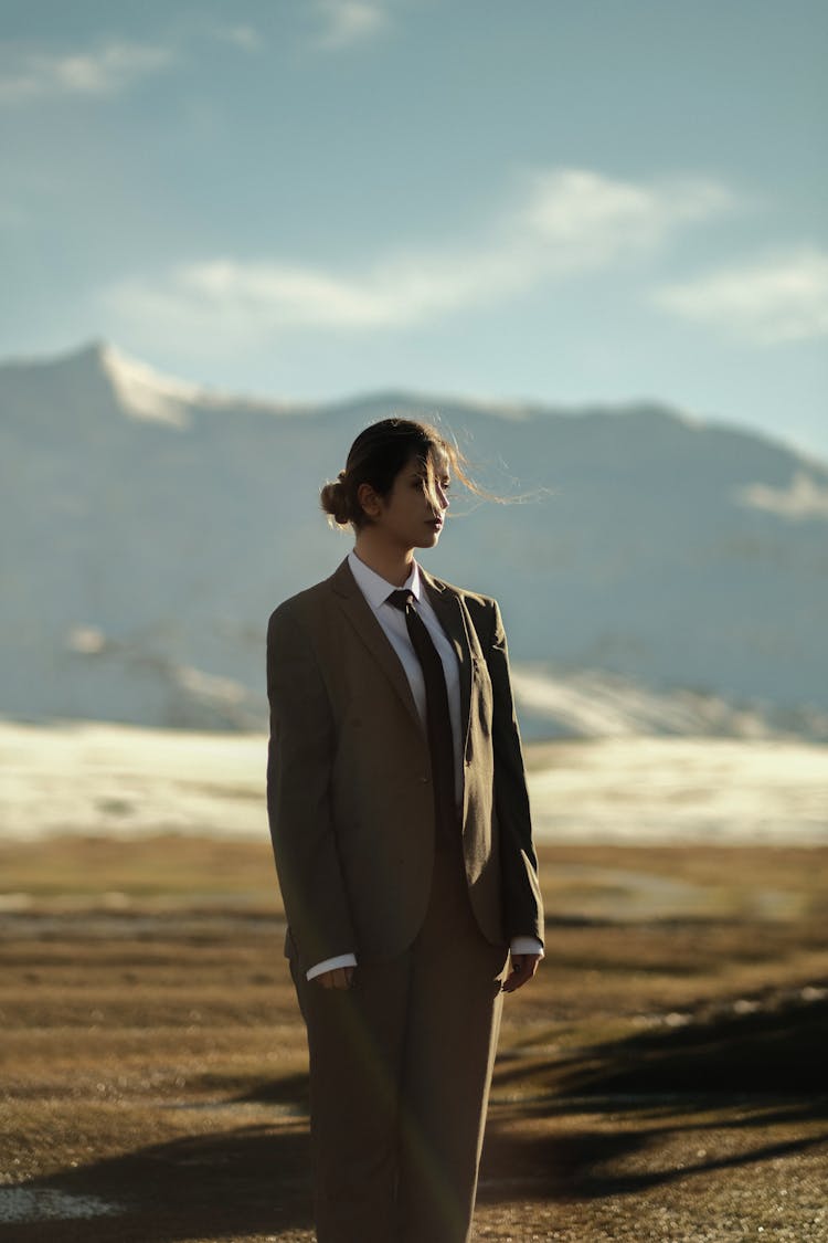 Woman In A Suit Standing On A Field With Mountains In The Background 