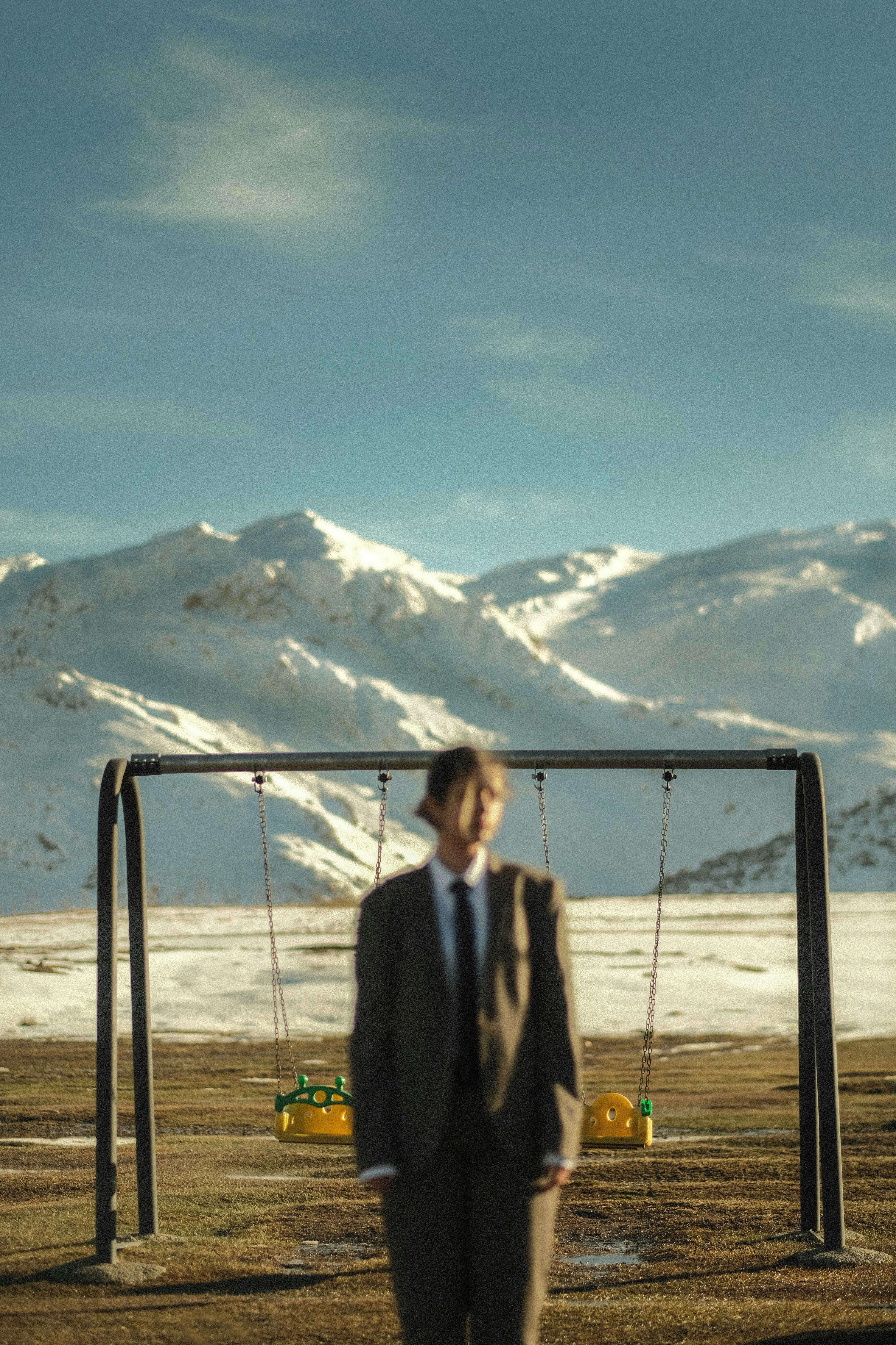 A person in a suit stands before swings in a snowy mountain range.