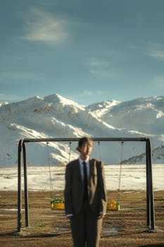 A person in a suit stands before swings in a snowy mountain range.