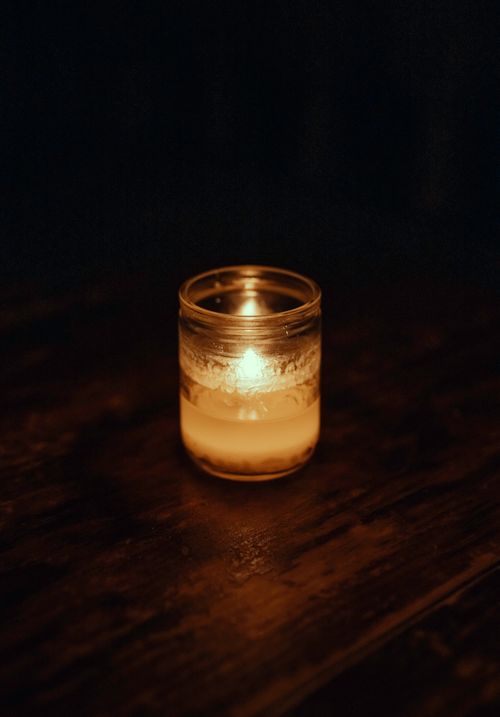 Free Warm candlelight glowing inside a glass jar, casting a soft ambiance on a wooden surface. Stock Photo