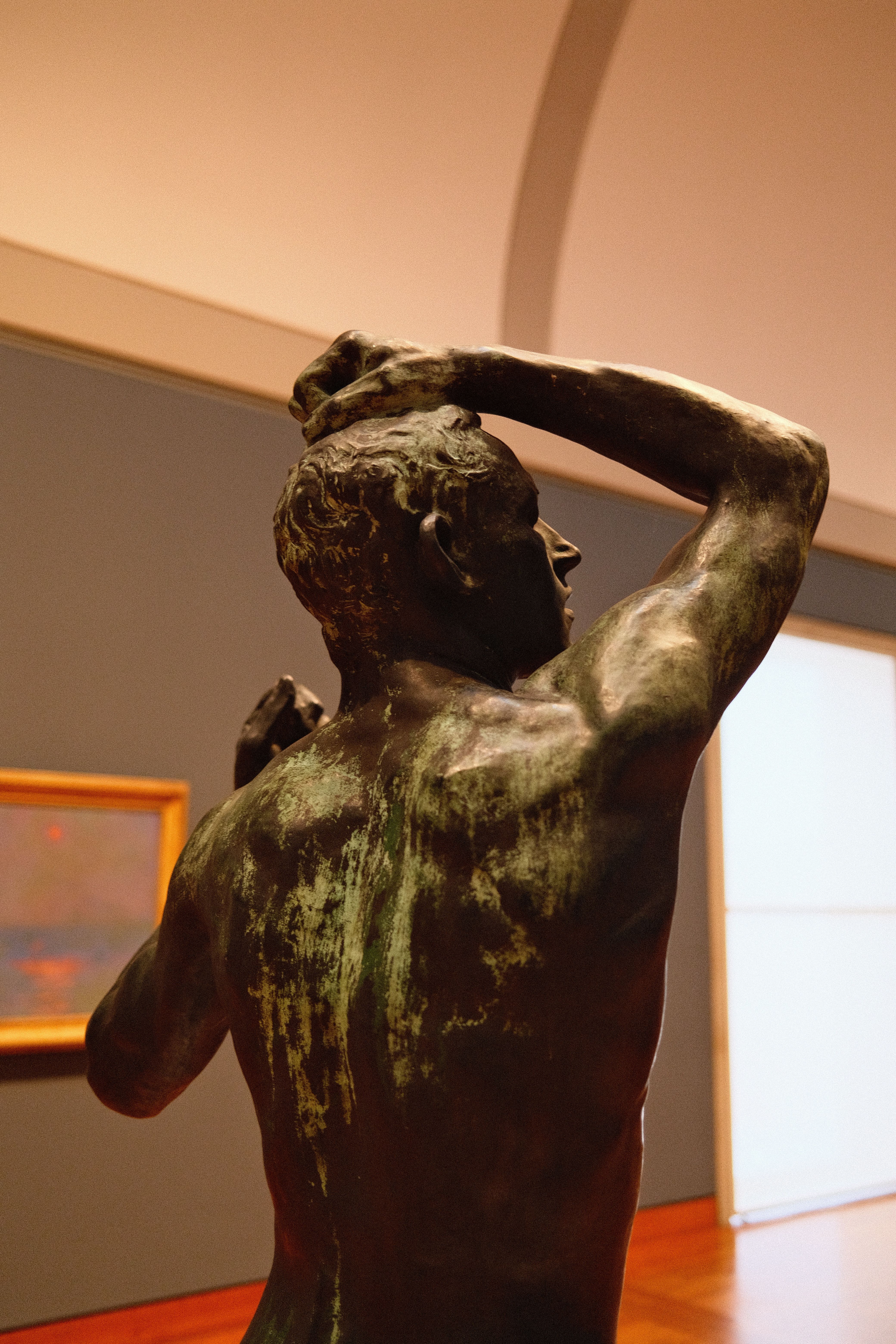 Back view of a bronze sculpture in a well-lit art gallery setting.