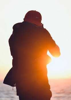 A photographer silhouetted against the bright sunset, capturing a scenic view.