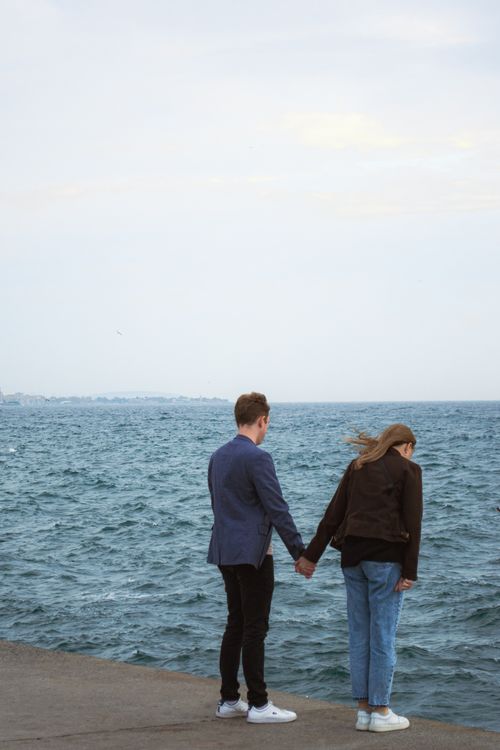 Free A couple romantic moment as they hold hands by the sea, feeling the ocean breeze. Stock Photo
