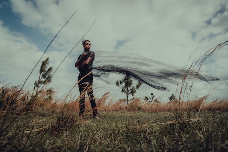 Man Standing On Grass And Holding Black Veil In Hands