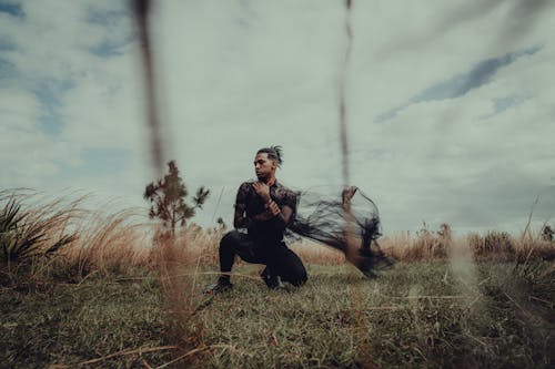 Man Kneeling on Grass Holding Black Fabric in Hands