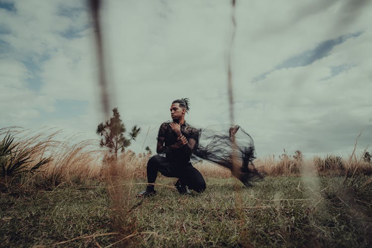 Man Kneeling On Grass Holding Black Fabric In Hands