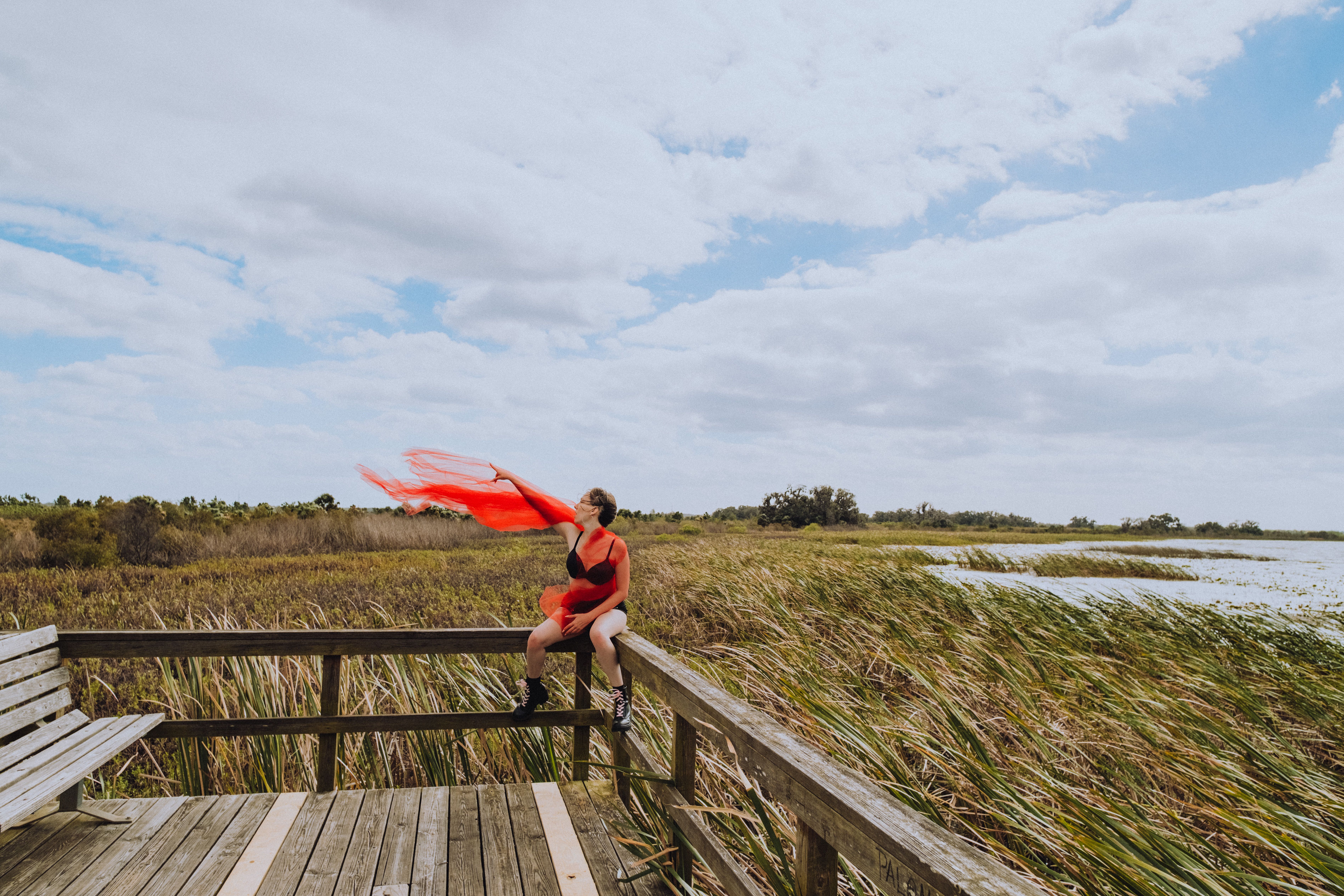 Young woman in red sarong enjoying nature from an observation deck, surrounded by marshland.