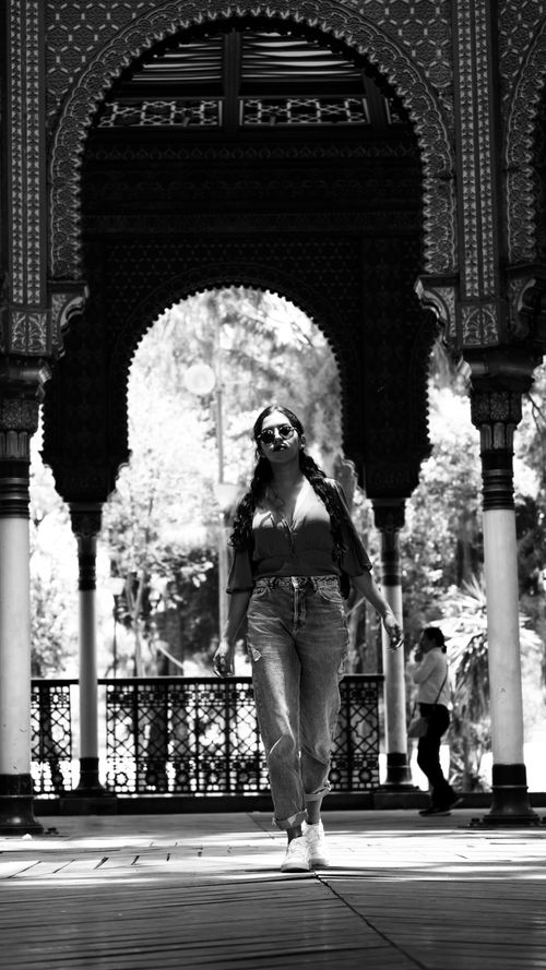 Free Monochrome image of a woman in casual attire walking under ornate arches. Stock Photo