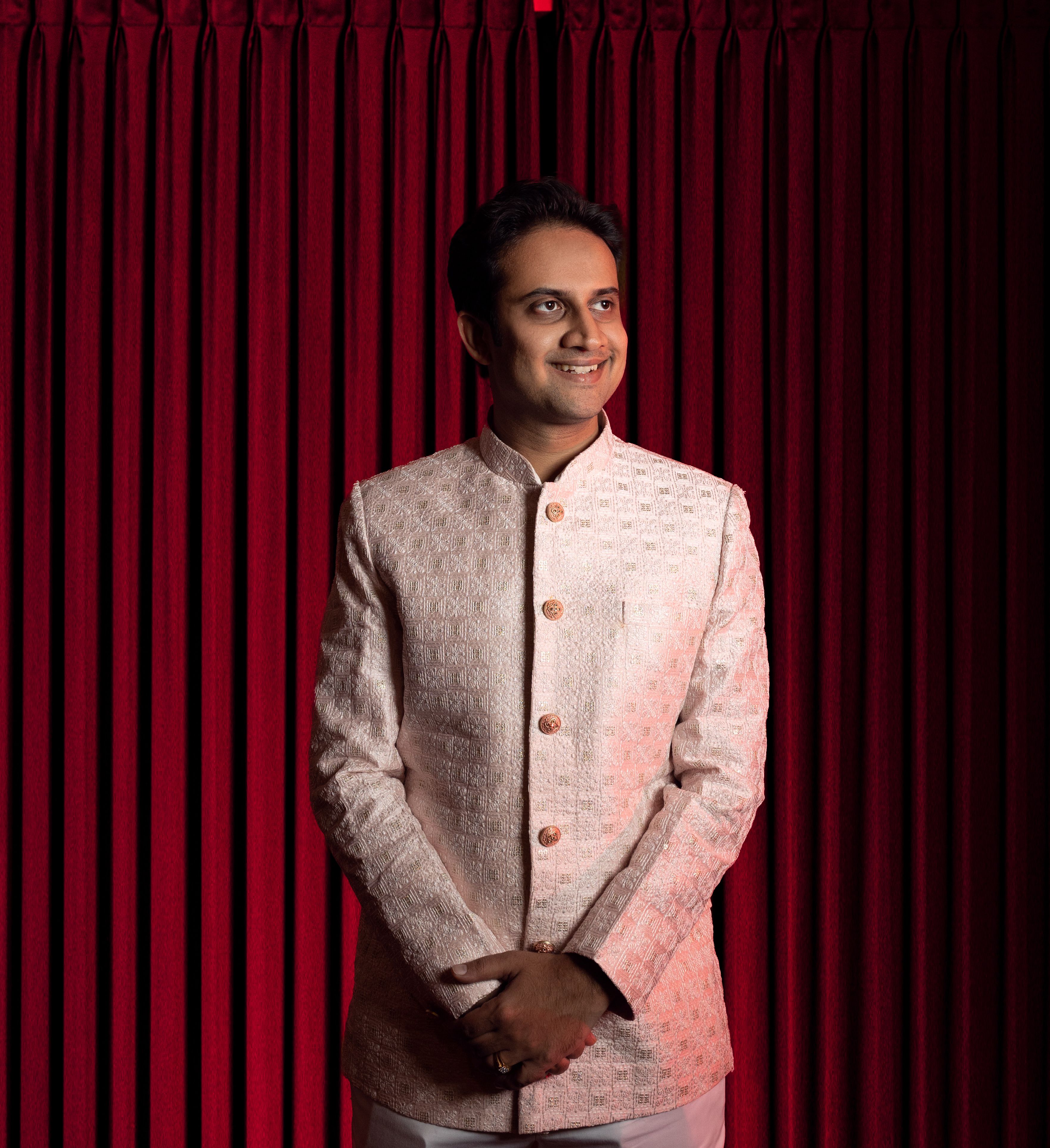 Portrait of a man wearing elegant traditional attire, standing confidently against a rich red curtain backdrop.