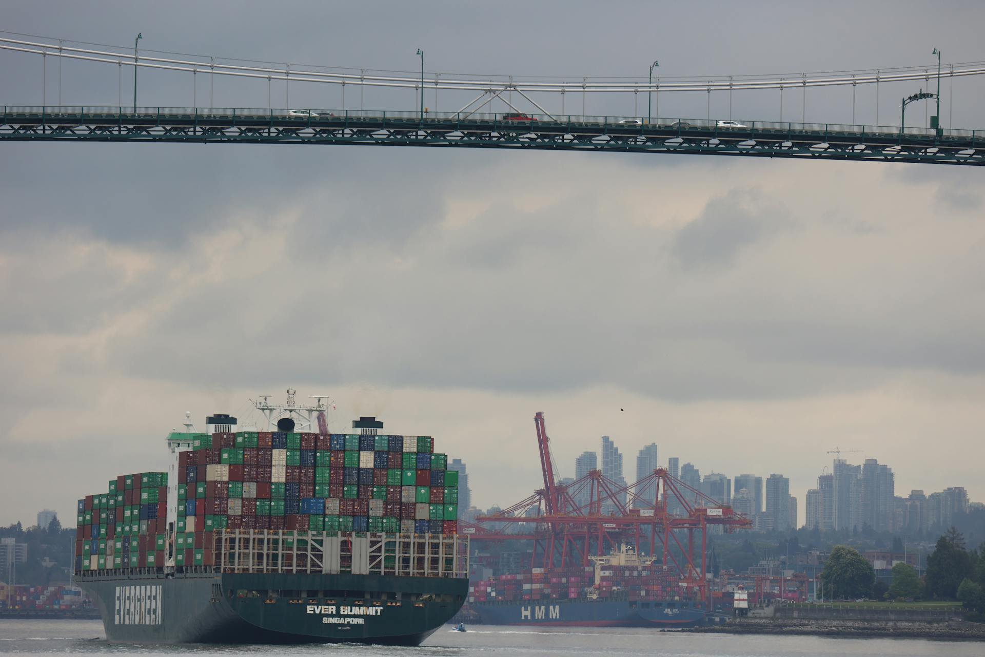 Container ship traverses under Lions Gate Bridge with Vancouver skyline backdrop, showcasing logistics and transport.