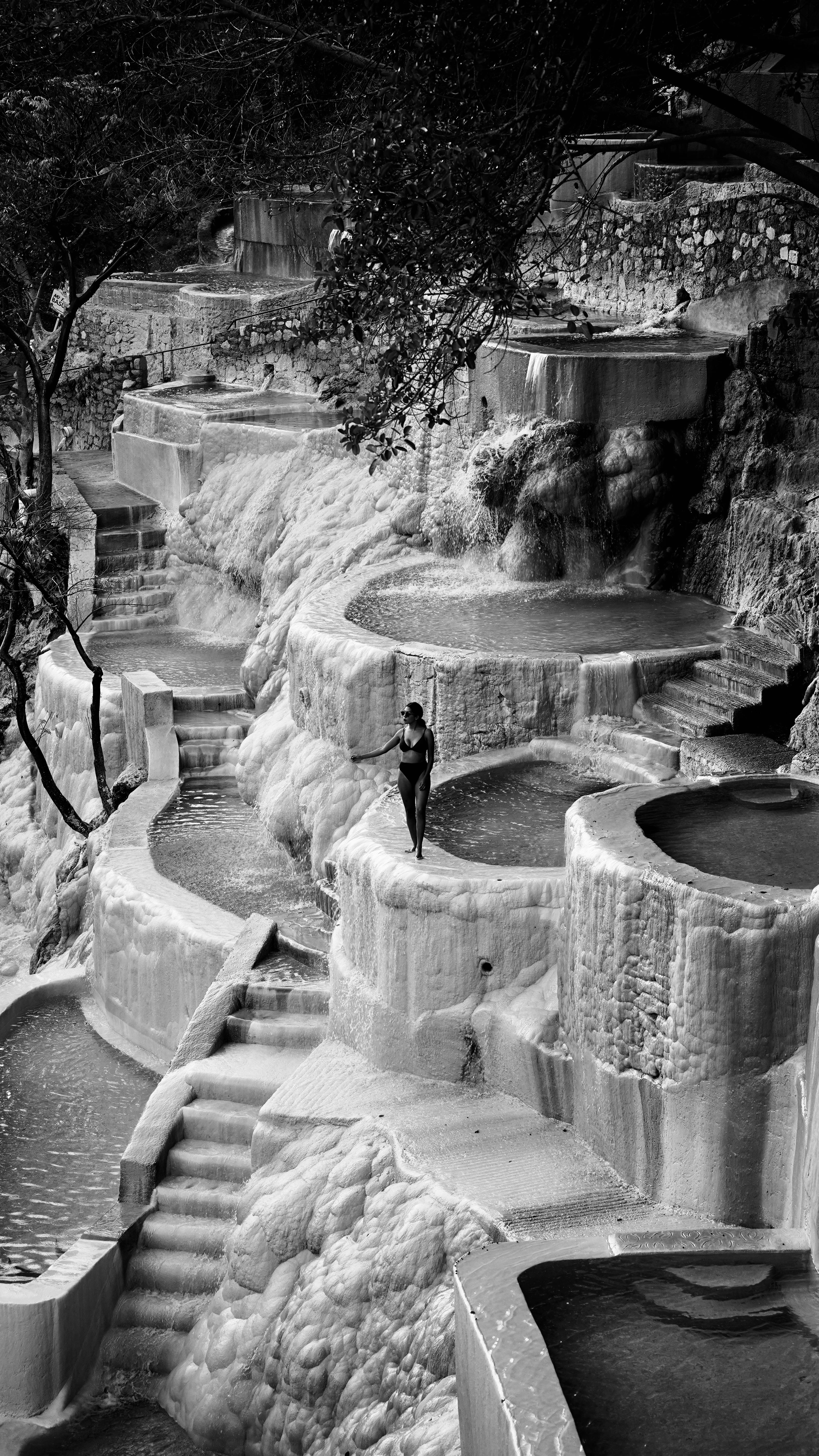 Elegant black and white photo of a woman standing amidst cascading pools and stairs.