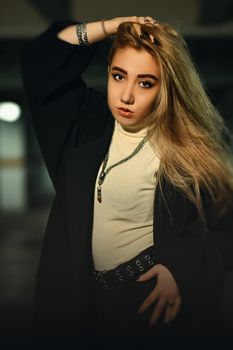 Portrait of a blonde woman in a black jacket and white turtleneck posing confidently indoors.