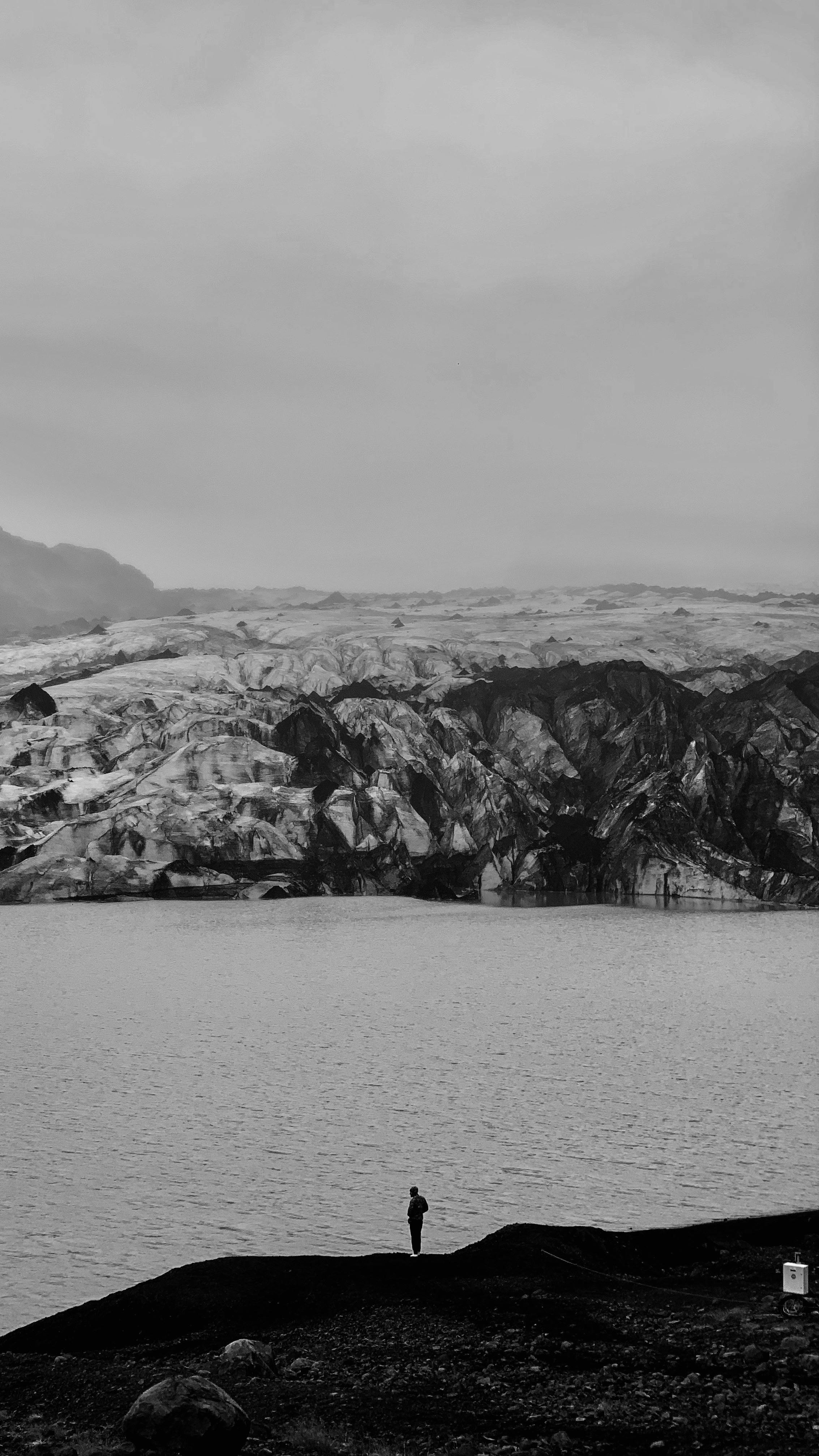 Black and white photo of a lone figure standing by a glacier edge, offering dramatic scenery.