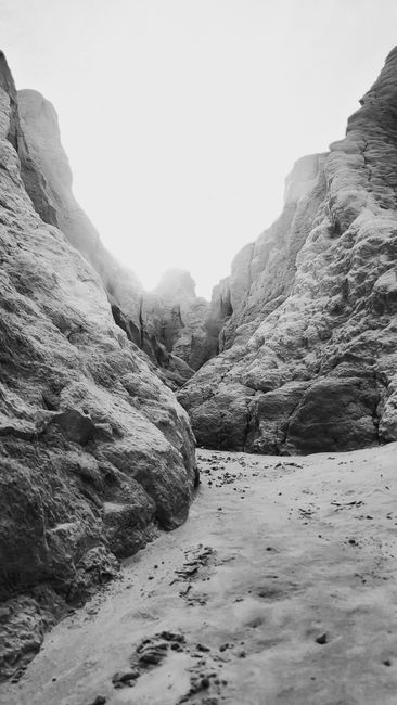 A dramatic black and white image of a narrow sandstone canyon with rugged rock formations.