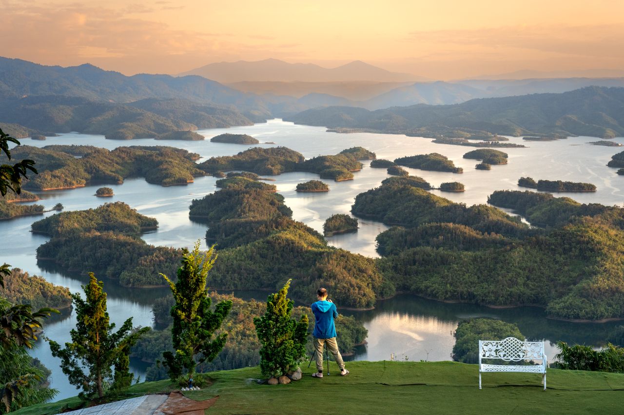 man in blue jacket overlooking a peaceful lake with lush islands at su