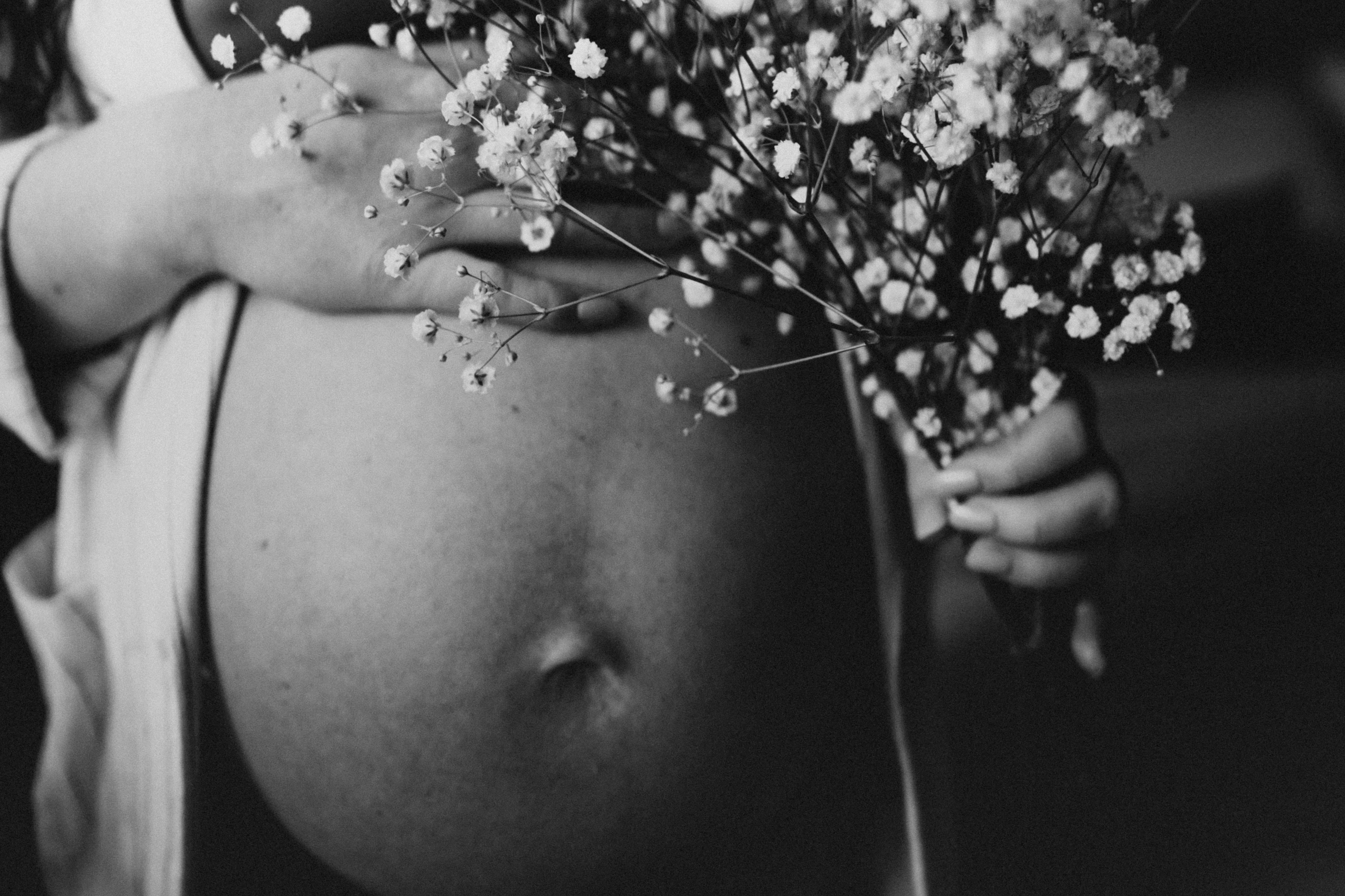 close up of pregnant woman stomach and flowers in hands